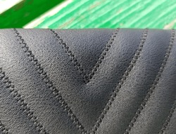 Black, leather, women's clutch with a triangular geometric print from seams, in the sun, on an old green bench (macro, top view, horizontal, texture).