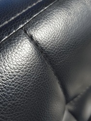 Black artificial leather with a small mesh print, with stitched convex squares - on the back of the armchair (macro, top-down view, diagonal, texture).