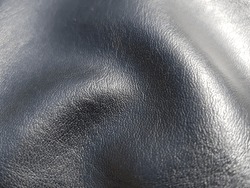 Black artificial leather with a small print, in the sun, in the folds (macro, texture).