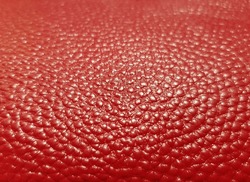 Red imitation leather with a small grainy mesh print (macro, angle, artificial lighting, texture).