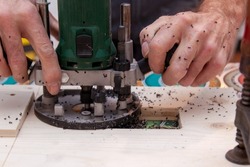 Man is milling a cutout in a panel. Person processes cutout with Fraser in a board. Hands is working with a template of wood for a milling machine. Male Hand of carpenter holds a carpentry tool. 