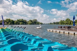 Colored Pedal boats at a wooden pier on a lake. Group of colorful pedal boats next to the wooden pier of Lake. Plastic white Swan Pedal Boat On Aasee (Aa-Lake) Muenster Germany. Active rest outdoor