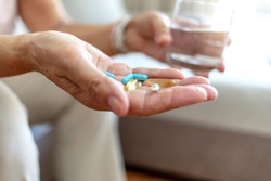 Close-up image of unrecognizable senior woman holding pills and glass of water, medicine and recovery treatment, copy space. Photo of a elderly woman taking daily medicine. Healthcare concept.
