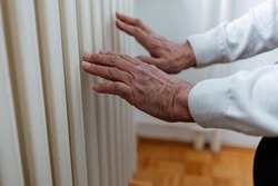 Man warms up hands over heater. Mens hands warms the frozen hands above a hot of the radiator, close up. Man getting warm up his hand over an electric radiator of heating at home.