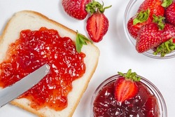 Toasts with strawberry jam for breakfast on white background. Top view. Ripen fresh strawberries and homemade strawberry jam, spread on bread by knife
