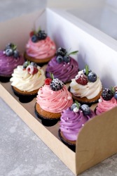 Beautiful cupcakes in a box. Festive birthday cupcakes. A box of cupcakes on a gray background. Colorful cupcakes with berries and cream. Dessert delivery 