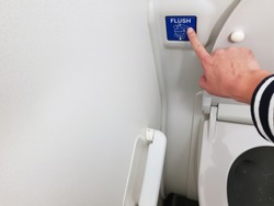 Asian men hand pressing blue flush button sign at the air plane lavatory to clean after use. Interior toilet design to match with small space inside the aircraft. 