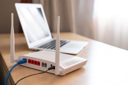 Selective focus at router. Internet router on working table with blurred computer at the background. Fast and high speed internet connection from fiber line with LAN cable connection.