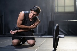 Young Caucasian men grab his arm and shoulder and feeling painful while weight lifting exercise inside of sport gym. Sport accident, overtrain. 
