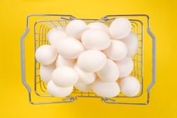 A full basket from the supermarket with white chicken eggs on a yellow background.The concept of healthy dietary nutrition,wholesale and retail sale or purchase of farm eggs. happy Easter.Top view