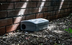 Grey Metal external rodent rat bait station outside against a brick wall close up.  Pest Control.