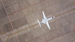 Top down aerial drone view of a private jet parked at an airfield. Business plane at airport terminal