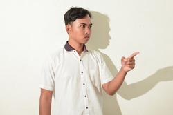 portrait of asian man glaring and pointing to the side. Indonesian man poses angry, glaring, and intimidating. asian man in white shirt isolated on white background
