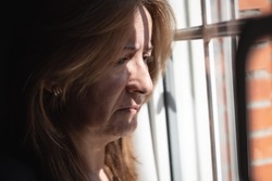 Crying woman looking out of a window after being assaulted by her partner at home.