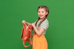 A joyful schoolgirl with long pigtails holds an open briefcase in her hands. green isolated background. the child is going to school with pleasure. getting an education.