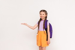 A little girl with a satchel behind her back holds your advertisement on a white isolated background on her hand.
