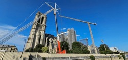 Restoration of Notre-Dame Cathedral, Paris, after major fire damage, with scaffolding, cranes and barriers; repairs of famous French cathedral Notre Dame in Paris under a clear blue sky

