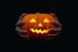 man's hands are holding a carved glowing pumpkin lantern with a creepy face. Halloween concept
