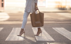 close up of woman legs walking on crosswalk. The woman is wearing shoes on high heels. Handbag in woman hand.