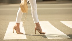 Close up of woman legs walking on crosswalk. The woman is wearing shoes on high heels.