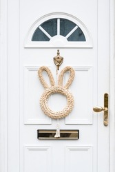 White wooden door with Easter bunny wreath. Minimalist Easter decoration