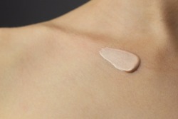 Closeup of a woman applying highlighting lotion to her neck and chest.