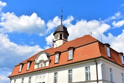 Old architectural building with white walls and red roof. Tower with a spire and an old clock at the top. Sunny summer day with blue sky. Kurnik, Poznan, Poland, June 2022.