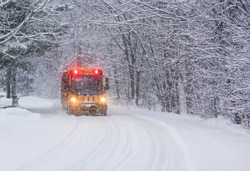 A school bus in a winter storm traveling on a deep snow covered rural road with stop lights flashing as it slows down to pick up students who were wishing for a 