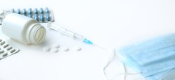 Medical topic. banner on white background with space for text. blue and white pills in package next to syringe with needle and protective mask. the concept of protection from the virus