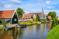 Picturesque idyllic De Rijp village in North Holland, Netherlands, view of characteristic wooden houses with red tiled roofs and flower beds and the church reflecting in a river