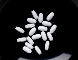 Several vitamin tablets on a black ceramic dish, close-up, top view.