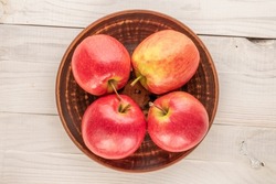 Four juicy red apples with a ceramic plate on a wooden table, close-up, top view.	