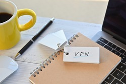 There's a word book on a desk with a cup of coffee and laptop pc. The word VPN is written in it. It's an abbreviation for Virtual Private Network.