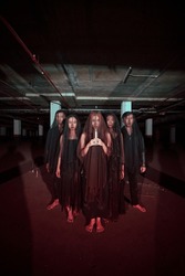 a group of devil worshipers in all black clothes and transparent veils holding candles together during a worship ritual in a building at night