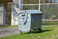 Standing iron garbage bin near fence on sunny day