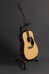 Six-string acoustic wooden guitar on a stand on a dark gray background. Vertical orientation, no people, copy space