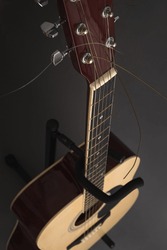 Six-string acoustic wooden guitar on a stand on a dark gray background. Vertical orientation, no people, copy space, selective focus