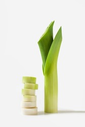 Sliced fresh raw leek wedges and a long stalk of leeks on a white background. Vertical