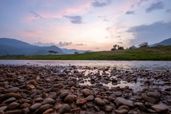 Wide view, low angle view, riverside scenery, mountains, evening sky, falling summer river, see small boulders The amount of water in the rivers in Thailand decreases every year.