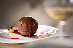 Chocolate sphere cake poured with hot chocolate on white plate in restaurant