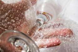 Material for packing fragile items for safe transportation. Close-up. Wine glass, hands pasking with bubble wrap
