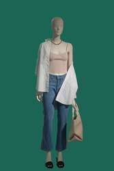 Full length image of a female display mannequin wearing pink top and blue jeans isolated on green background