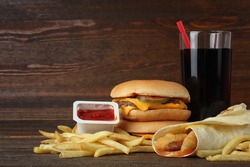Big appetizing hamburger with ketchup and French fries with a coke on the fabric on a brown wooden table