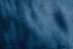 Dark blue rough surface, textured wall covered with old peeling off plaster. Texture and background photo with a spot of light and shadows