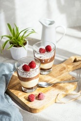 Three-layer mousse dessert made of chocolate and vanilla, decorated with fresh raspberries and coconut flakes in glasses on the table. Brunch, dessert for lovers