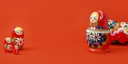 Closed nesting dolls on red background banner with copy space. Bigger and smaller similar wooden toys.