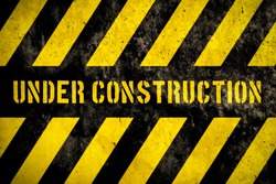 Under construction warning sign with yellow and dark stripes painted over concrete wall coarse facade as texture background. Concept for do not enter the area, caution, danger, construction site.