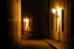 Old lanterns illuminating a dark alleyway medieval street at night in Prague, Czech Republic. Low key photo with brown yellow tones from the lanterns as single light sources against the dark shadows