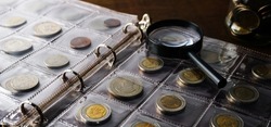 Old collectible coins on a wooden table. Dark background. Banner. Numismatics, Coins in the album. Magnifying glass, Selective focus.