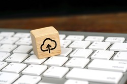 Cloud computing upload icon on wooden cube on a white computer keyboard. Remote download technology concept.